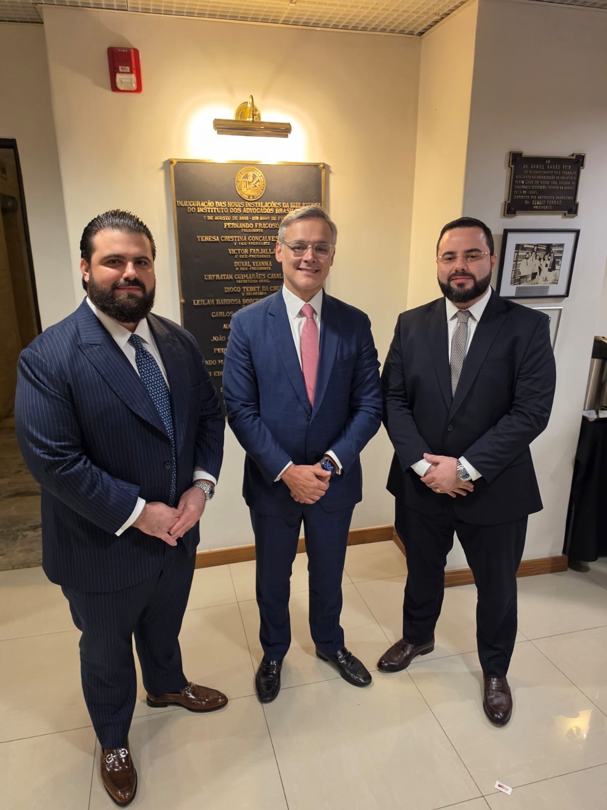 Filipe Maia Broeto ao lado de dois advogados diante da placa da biblioteca do Instituto dos Advogados Brasileiros