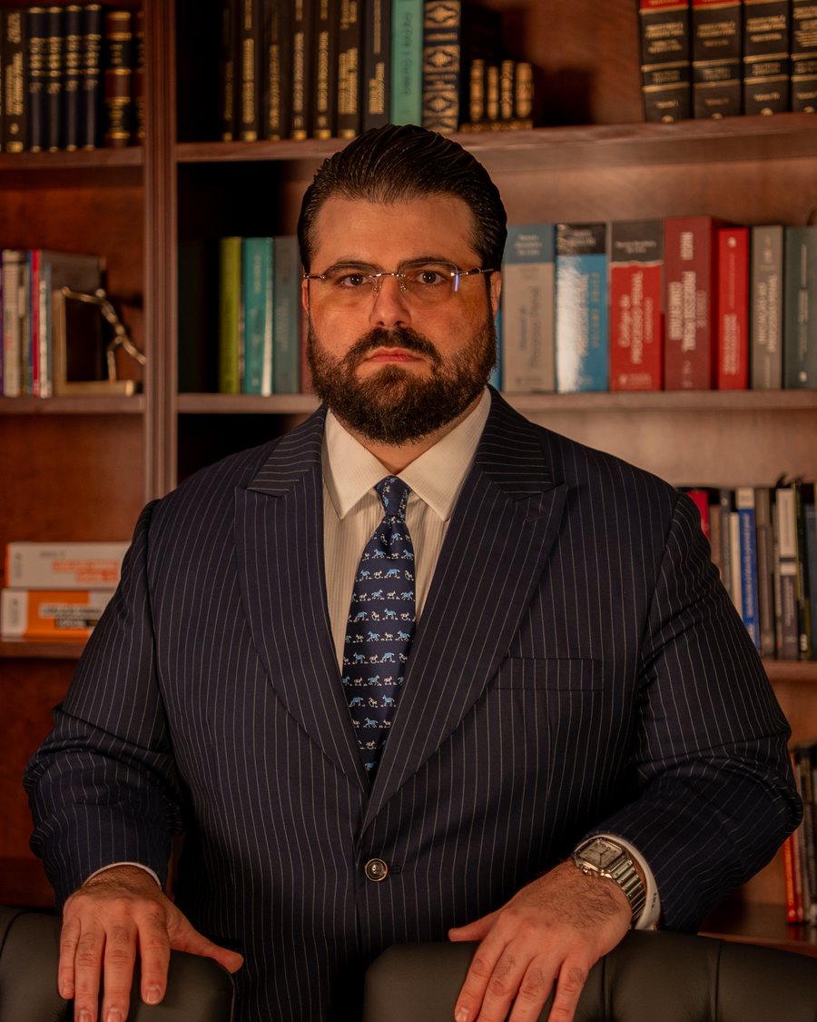 Retrato do advogado criminalista Filipe Maia Broeto, de terno risca de giz, diante de estante de livros jurídicos